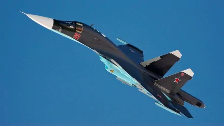 HD desktop wallpaper featuring a military Sukhoi Su-34 fighter jet soaring against a clear blue sky.