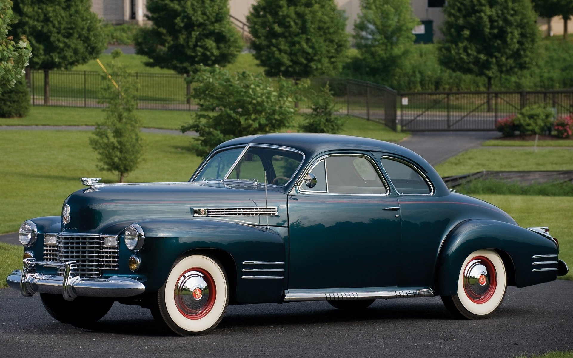 HD desktop wallpaper featuring a classic 1941 Cadillac Sixty-Two Coupe parked on a driveway with greenery and buildings in the background.
