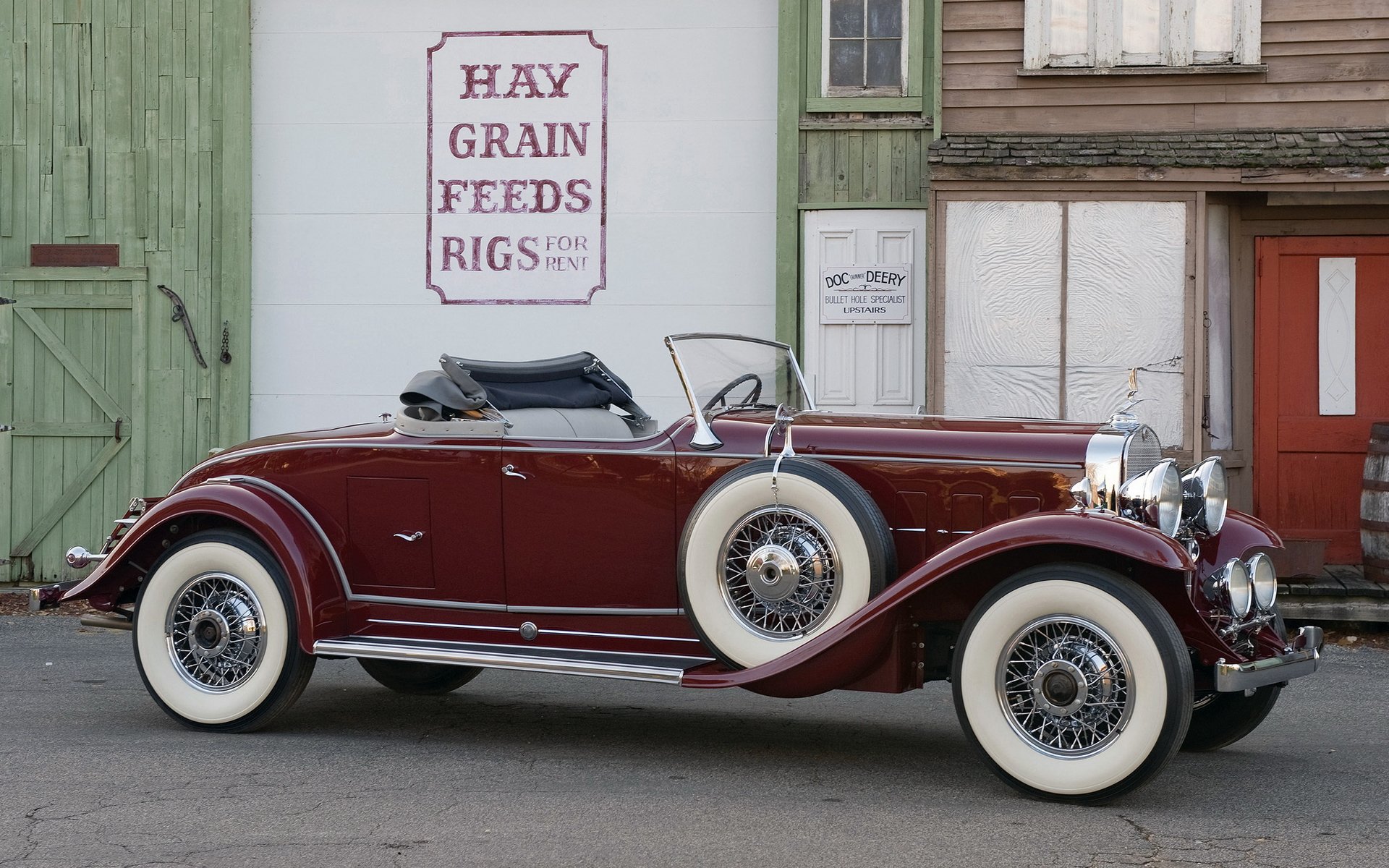 HD desktop wallpaper featuring a classic 1931 Cadillac V12 convertible parked in front of rustic buildings with vintage signage.