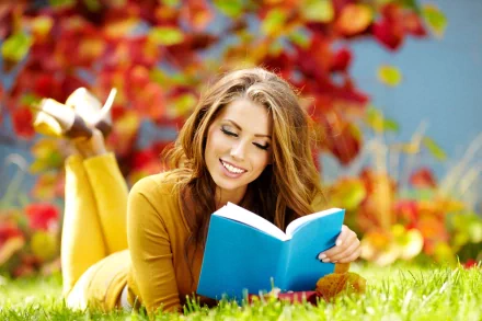 A stylish woman enjoys a book while lounging on the grass, surrounded by vibrant fall colors, creating a warm and inviting mood in this 4K Ultra HD wallpaper.
