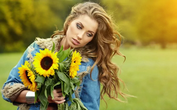 A beautiful woman with long wavy hair holds a bouquet of sunflowers, set against a soft green and yellow blurred background in 4K Ultra HD quality.