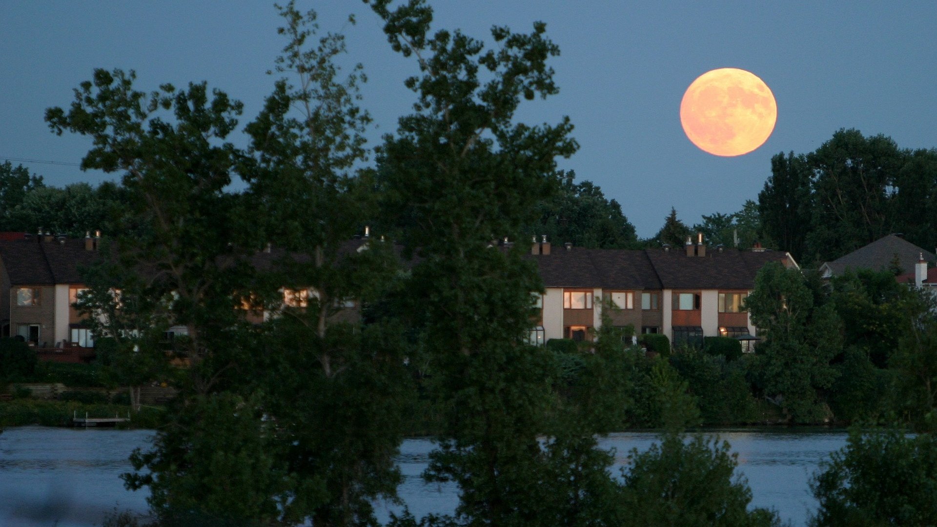 HD PC desktop wallpaper and background: nature scene with a full moon rising over a tree-lined lakeshore and silhouetted suburban homes at dusk.