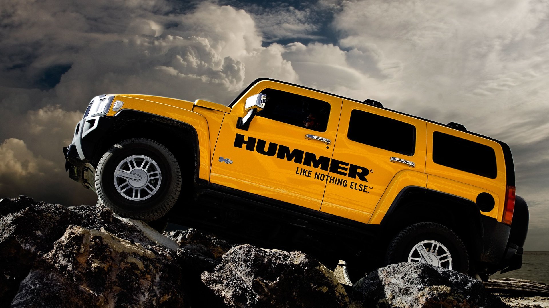 Yellow Hummer climbing rocky terrain beneath dramatic clouds — HD PC desktop wallpaper and background.