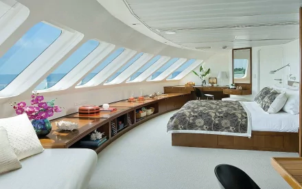 HD desktop wallpaper showcasing a modern, man-made room with large angled windows, a curved wooden shelf, and a cozy bed with patterned bedding.