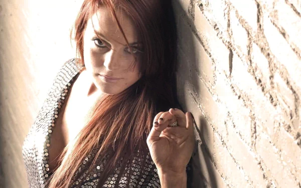 HD desktop wallpaper featuring celebrity Lindsay Lohan leaning against a textured wall with soft lighting highlighting her face and hair.