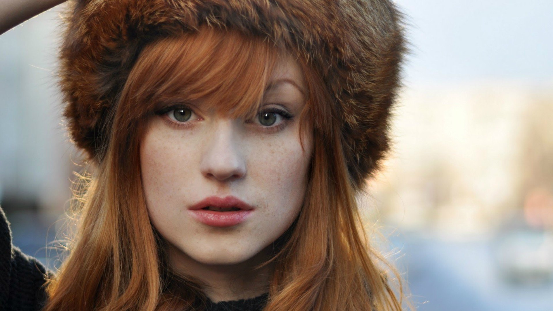 A woman with striking red hair and a fur hat gazes directly at the camera, creating a captivating atmosphere in this HD desktop wallpaper and background.