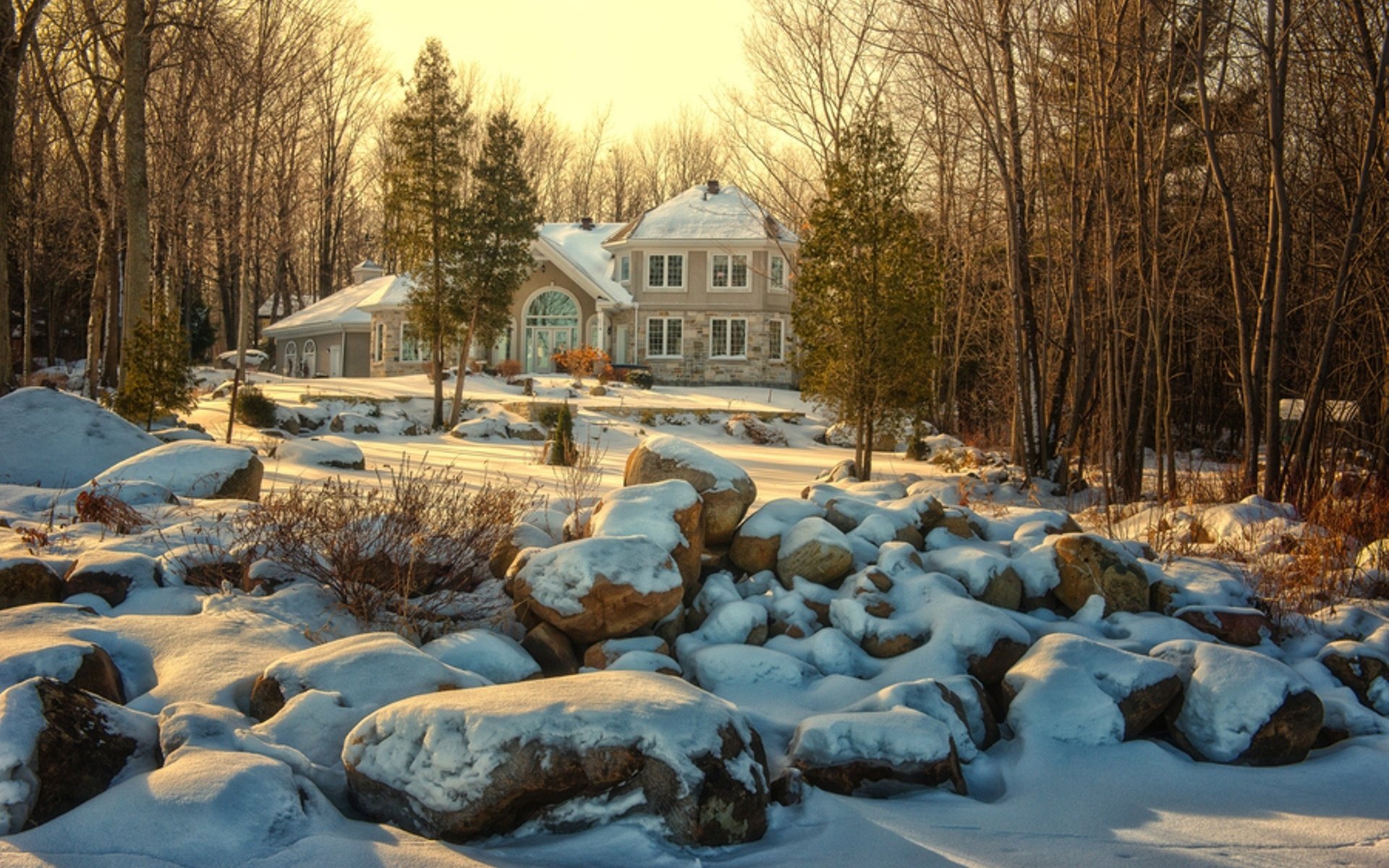 HD desktop wallpaper of a man-made mansion surrounded by snow-covered rocks and bare trees in a serene winter landscape.