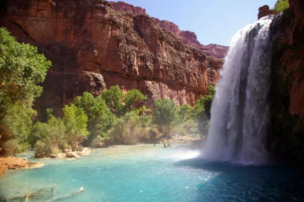 A stunning waterfall cascades into a clear blue pool, framed by lush greenery and towering mountains, creating a breathtaking natural scene for an HD desktop wallpaper.