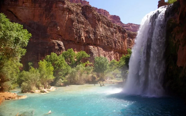 A stunning waterfall cascades into a clear blue pool, framed by lush greenery and towering mountains, creating a breathtaking natural scene for an HD desktop wallpaper.