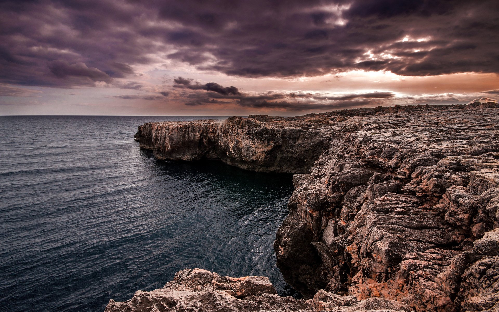 Nature, ocean HD PC desktop wallpaper and background: rugged rocky cliffs plunging into a dark sea beneath a brooding, cloud-filled sunset sky.