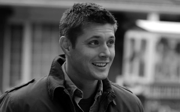A captivating HD desktop wallpaper featuring Jensen Ackles smiling, dressed in a casual coat, set against a blurred background.