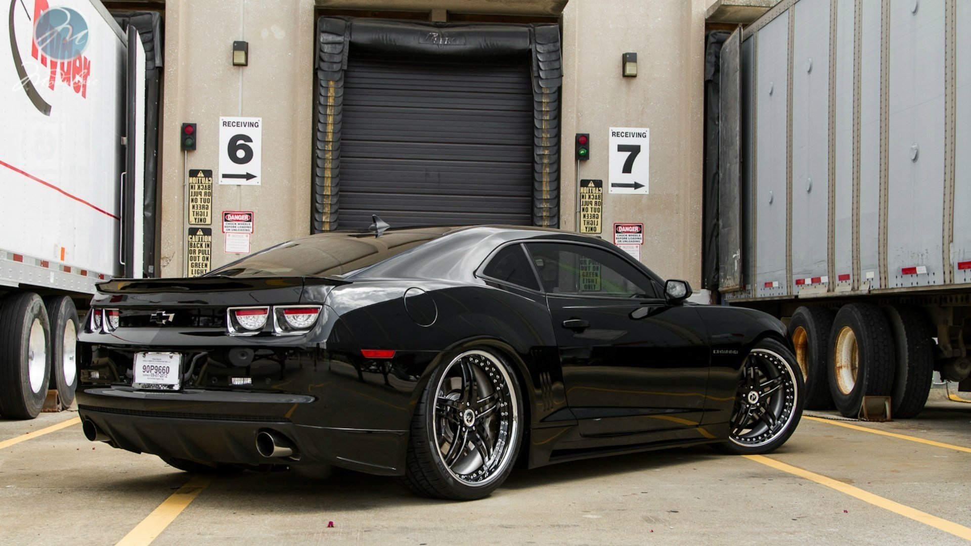 HD desktop wallpaper featuring a sleek black Chevrolet Camaro SS parked between loading docks, highlighting its sporty design and polished finish.
