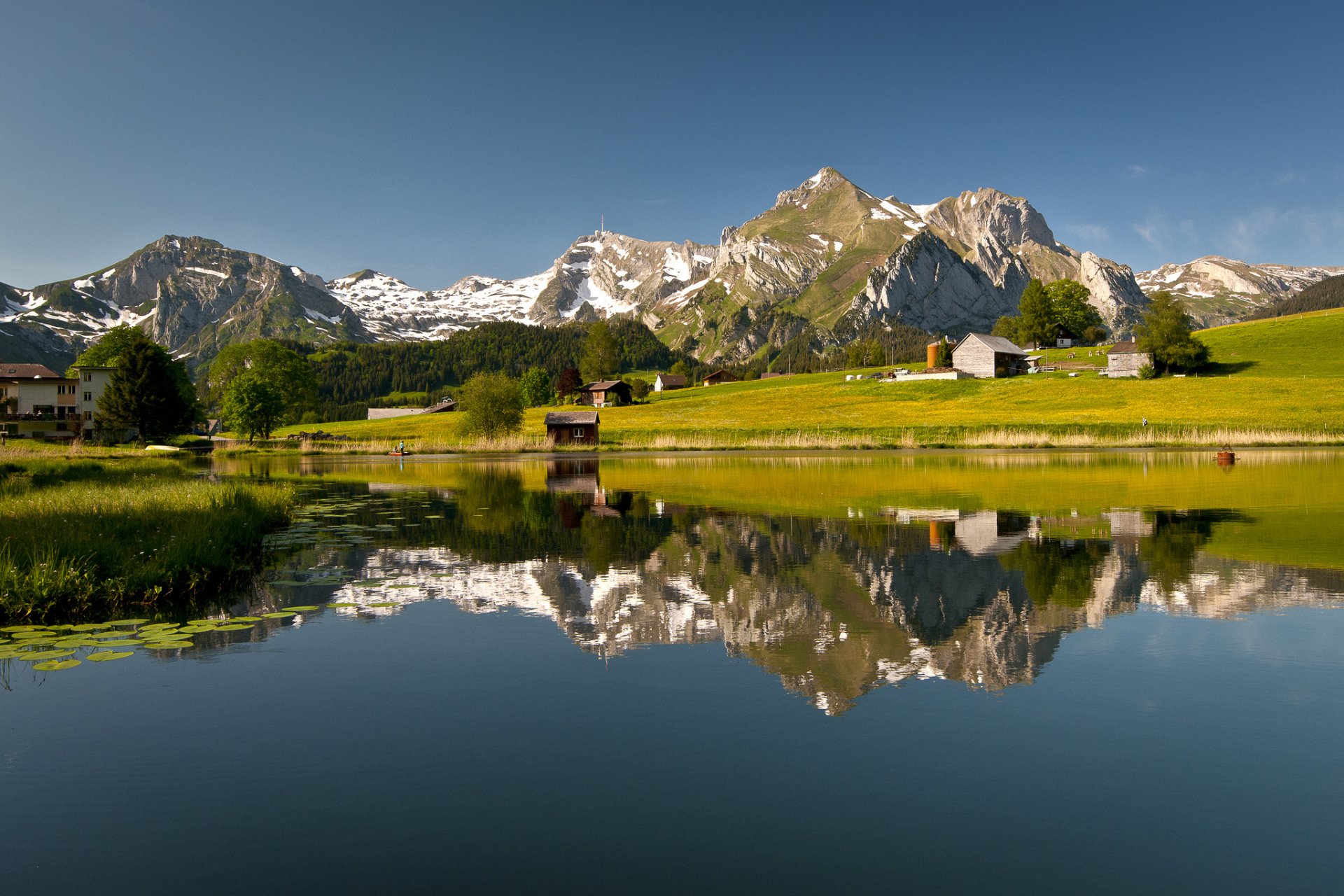 HD PC desktop wallpaper: Swiss mountains, green meadows and chalets mirrored in a glassy lake — nature photography capturing a crisp mountain reflection.
