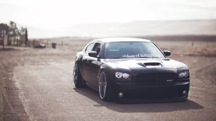 HD PC desktop wallpaper featuring a black Dodge Charger SRT8 parked on a deserted road with a blurred, mountainous background.