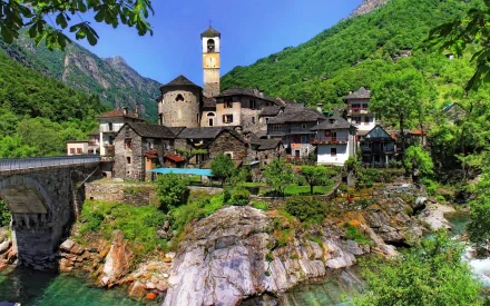 HD desktop wallpaper showing the man-made town of Lavertezzo in Ticino, nestled among green hills with stone buildings and a clock tower by a rocky river.
