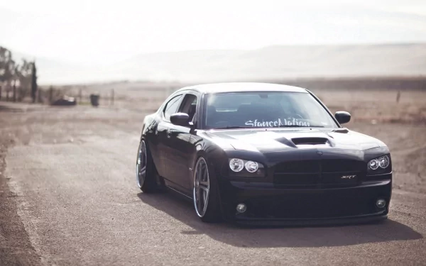 HD PC desktop wallpaper featuring a black Dodge Charger SRT8 parked on a deserted road with a blurred, mountainous background.