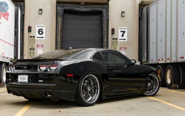 HD desktop wallpaper featuring a sleek black Chevrolet Camaro SS parked between loading docks, highlighting its sporty design and polished finish.