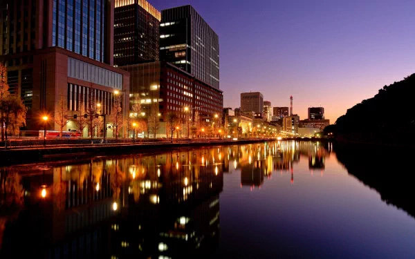 HD desktop wallpaper featuring a man-made Tokyo cityscape at dusk, with illuminated buildings and their reflections glowing on the calm water.