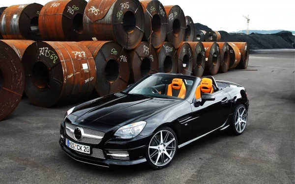 Vehicle: black Mercedes‑Benz SLK‑Class convertible with orange seats parked by stacked steel coils — HD PC desktop wallpaper background