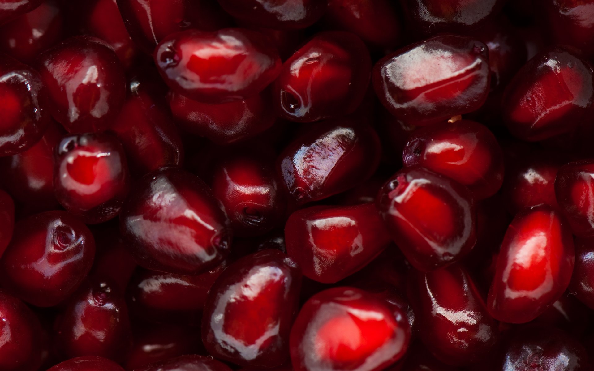 Close-up HD PC desktop wallpaper of vibrant, glossy red pomegranate seeds showcasing their juicy texture and rich color.
