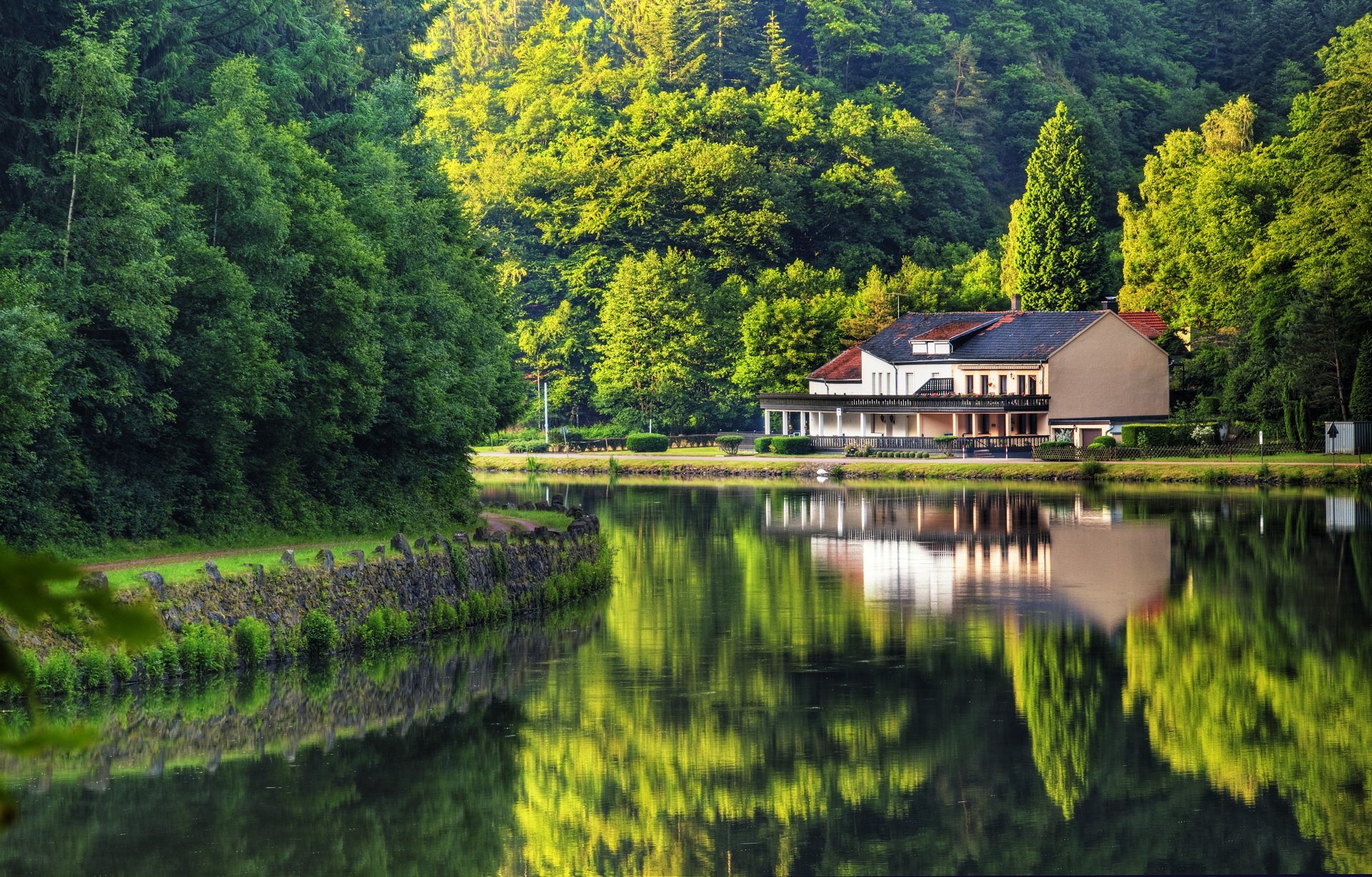 A serene landscape featuring a reflective lake, surrounded by lush greenery, with a modern house on the shore, captured in vibrant detail for a 4K Ultra HD desktop wallpaper.