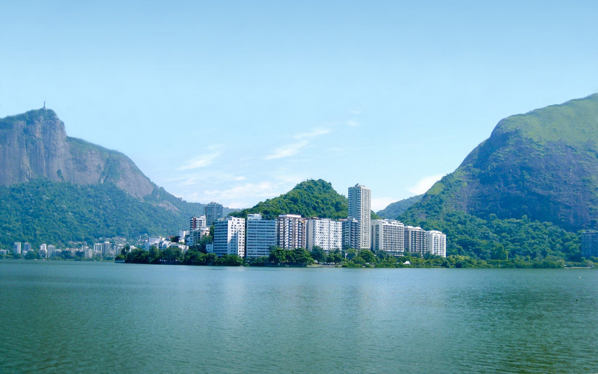 2K Quad HD PC desktop wallpaper: man-made waterfront skyline of Rio de Janeiro, apartment blocks along a calm lagoon between green hills and a distant Christ the Redeemer.