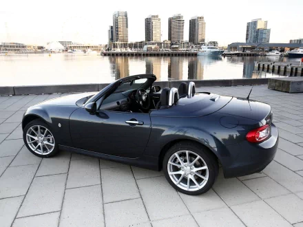 HD PC desktop wallpaper showcasing a sleek gray Mazda MX-5 convertible parked on waterfront pavement with modern buildings in the background.