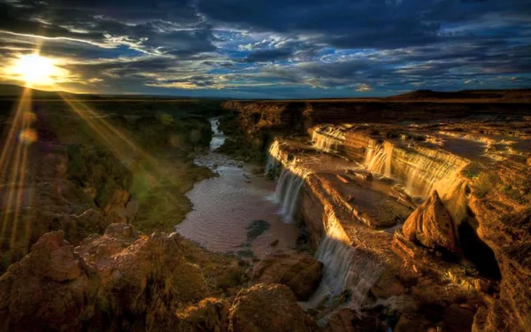 HD desktop wallpaper showcasing a stunning Arizona waterfall at sunset, with dramatic clouds and rugged natural landscape.