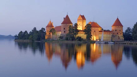 HD desktop wallpaper featuring the illuminated Trakai Island Castle reflected on calm water under a twilight sky.