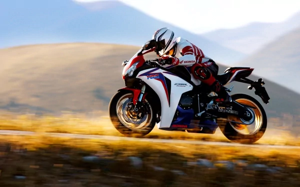 A Honda CBR motorcycle accelerates dynamically on a winding road, set against a backdrop of rolling hills, creating a striking HD desktop wallpaper.