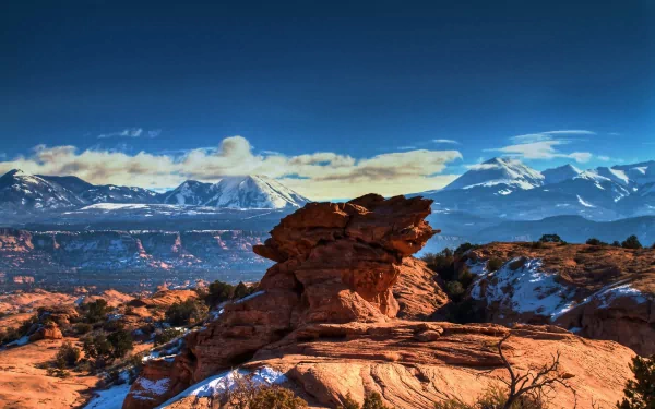 HDR landscape of Utah’s Moab desert featuring red rock formations and snow-dusted mountains under a vibrant blue sky, captured as an HD PC desktop wallpaper.