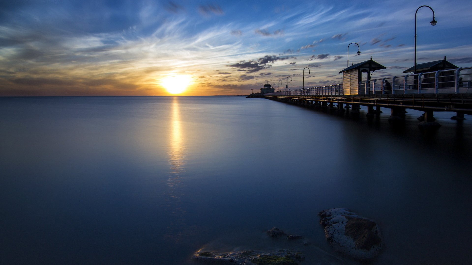 HD desktop wallpaper showcasing a man-made pier extending into calm waters during a vibrant sunset with a colorful sky.