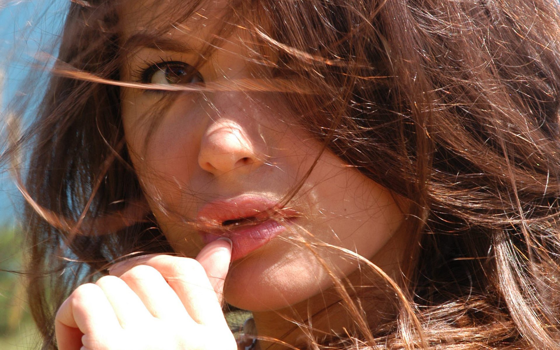 A woman with flowing hair, some strands covering her face, gazes intently while lightly touching her lips. This high-definition desktop wallpaper captures an expressive, intimate moment.