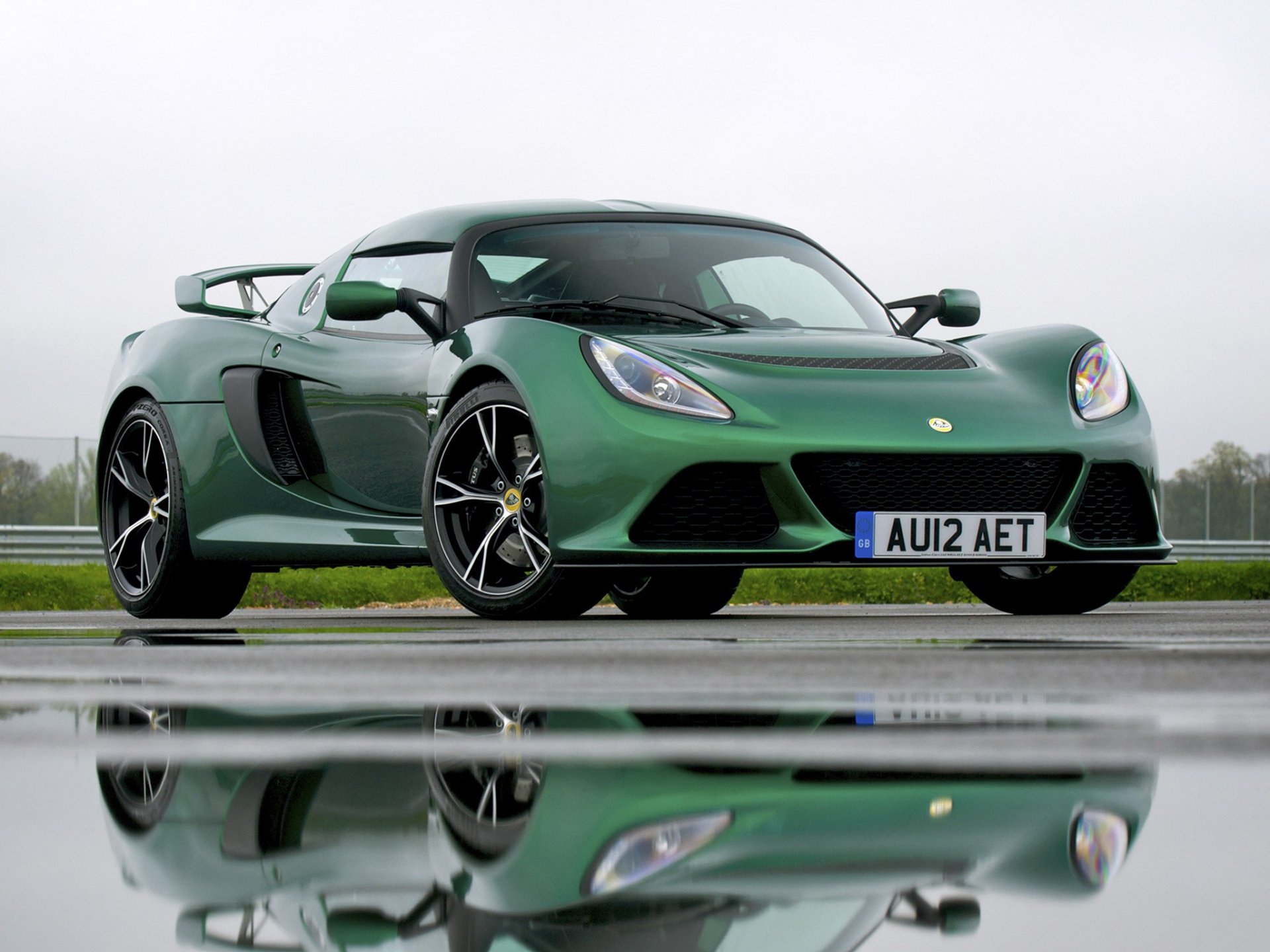 A sleek green Lotus Exige sports car with black accents, showcased on a wet surface reflecting the vehicle, captured as an HD desktop wallpaper.