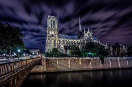 HD desktop wallpaper showcasing the illuminated Notre-Dame de Paris at night, highlighting the iconic religious architecture under a dramatic cloudy sky.