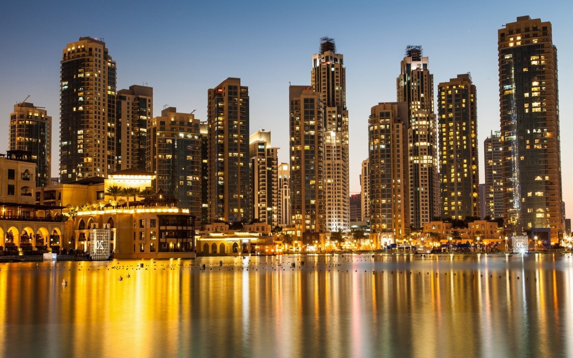 HD desktop wallpaper showcasing the illuminated man-made skyline of Dubai at night, reflecting beautifully over calm waters.