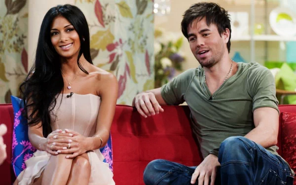 A vibrant HD desktop wallpaper featuring Enrique Iglesias and a female guest, both seated and engaged in conversation against a colorful backdrop.
