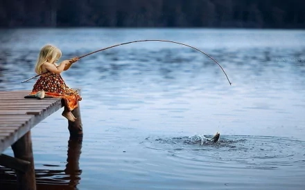 A child sits on a dock fishing, reeling in a catch from the calm lake, captured in this HD PC desktop wallpaper showcasing serene outdoor photography.