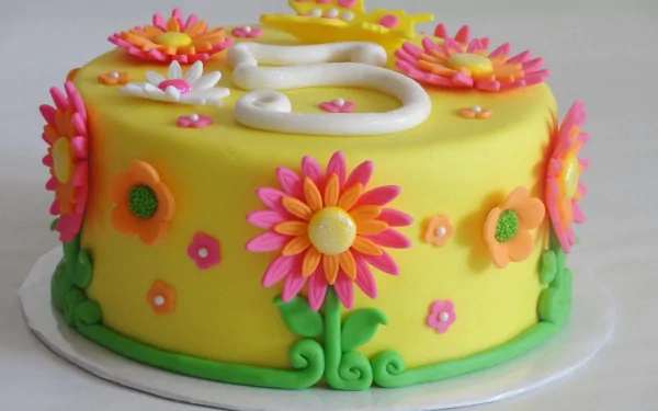 HD desktop wallpaper of a vibrant yellow cake decorated with colorful fondant flowers and a white number five on top.