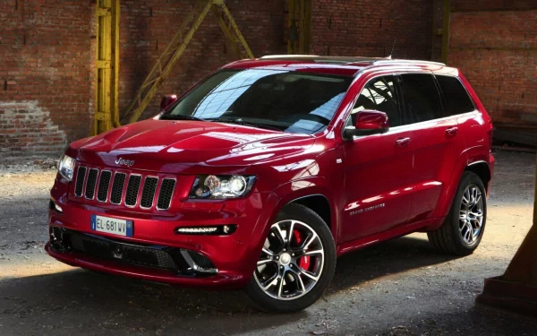 A red Jeep Grand Cherokee SRT8 parked in an industrial setting, showcased as an HD PC desktop wallpaper and background.