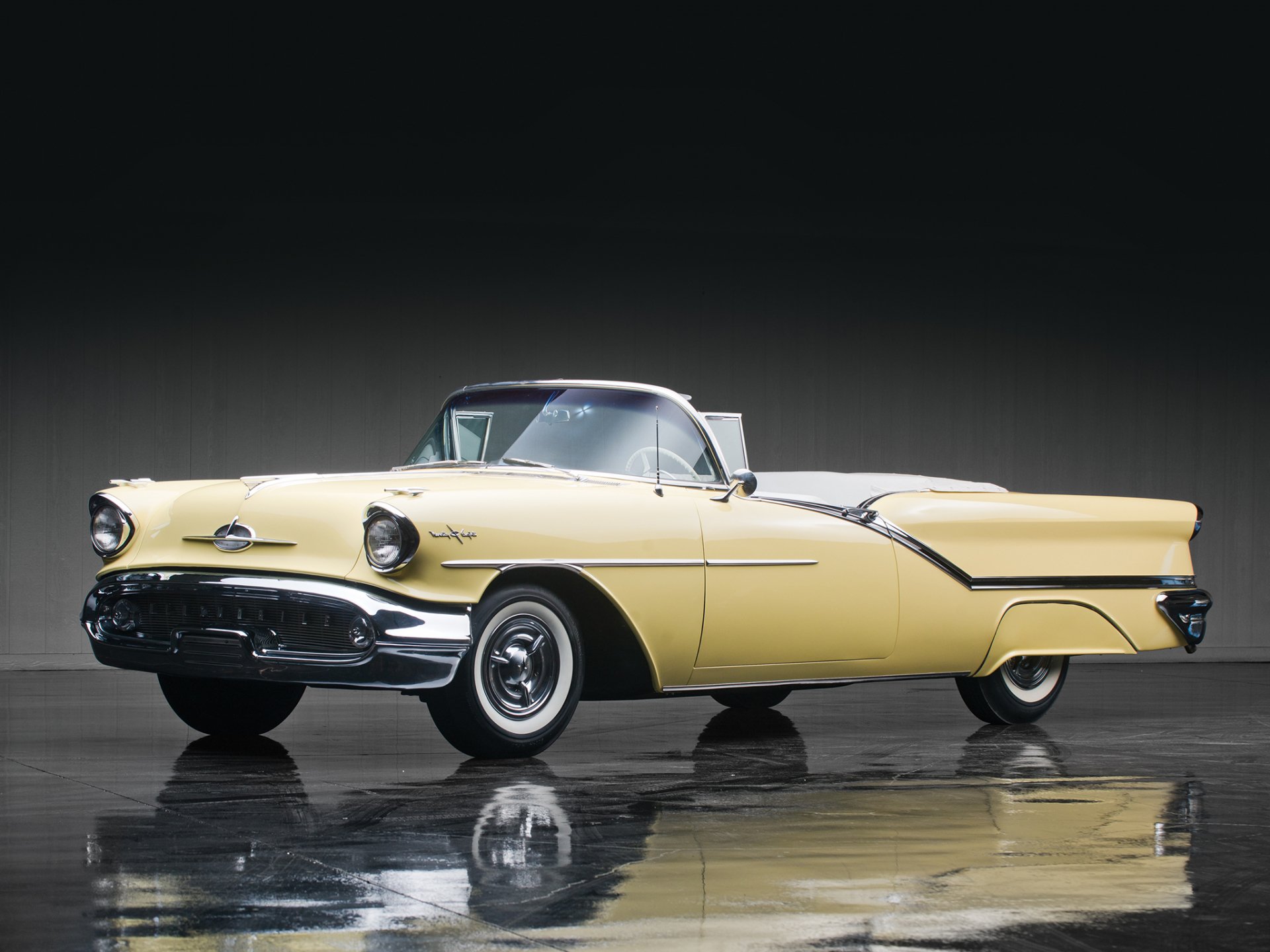 1957 yellow Oldsmobile Starfire convertible shown with a clear reflection on a dark, glossy surface in this HD desktop wallpaper and background image.