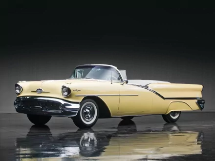 1957 yellow Oldsmobile Starfire convertible shown with a clear reflection on a dark, glossy surface in this HD desktop wallpaper and background image.
