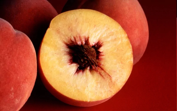 HD PC desktop wallpaper featuring a close-up of a ripe peach cut in half, highlighting its vibrant colors and texture against a rich red background.