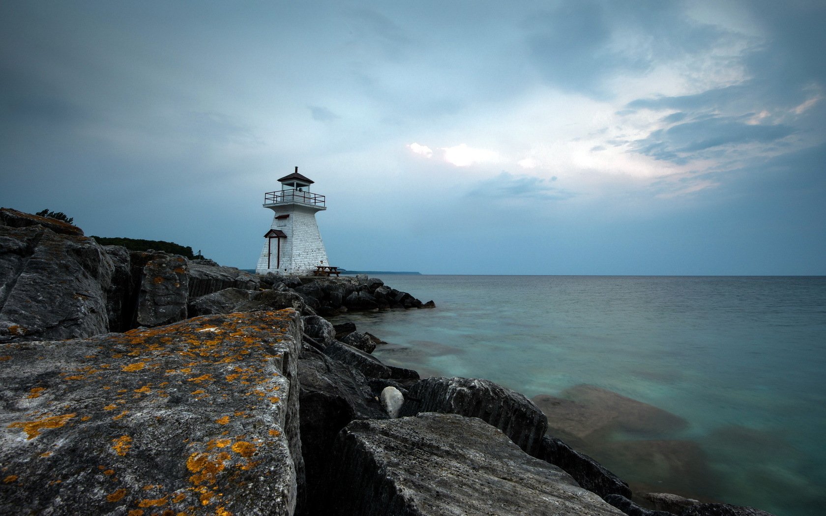 HD PC desktop wallpaper and background: man-made lighthouse on a rocky jetty under a moody sky, calm sea stretching to the horizon.