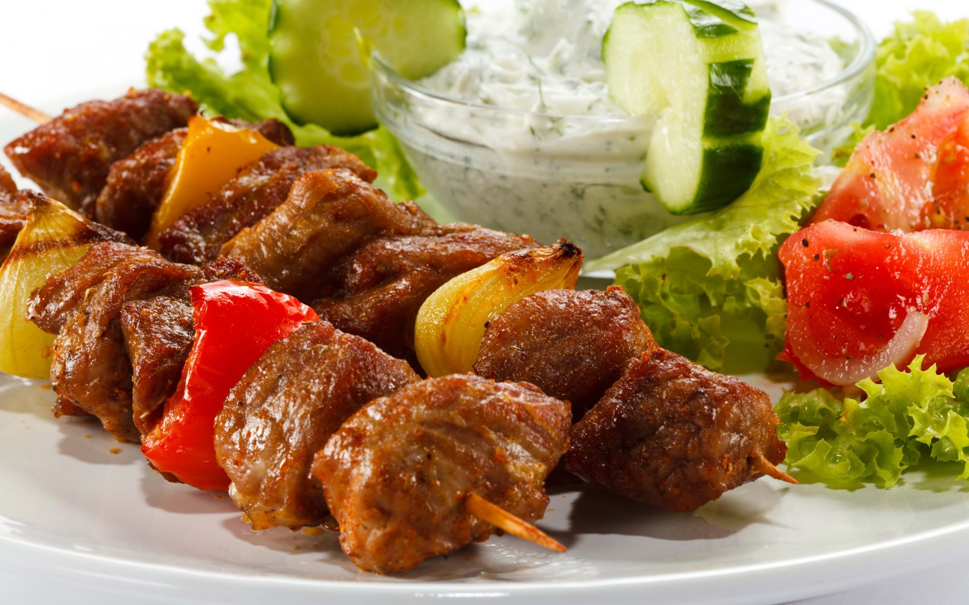 HD desktop wallpaper featuring juicy barbecue meat skewers with colorful bell peppers, served alongside fresh salad and cucumber yogurt dip.