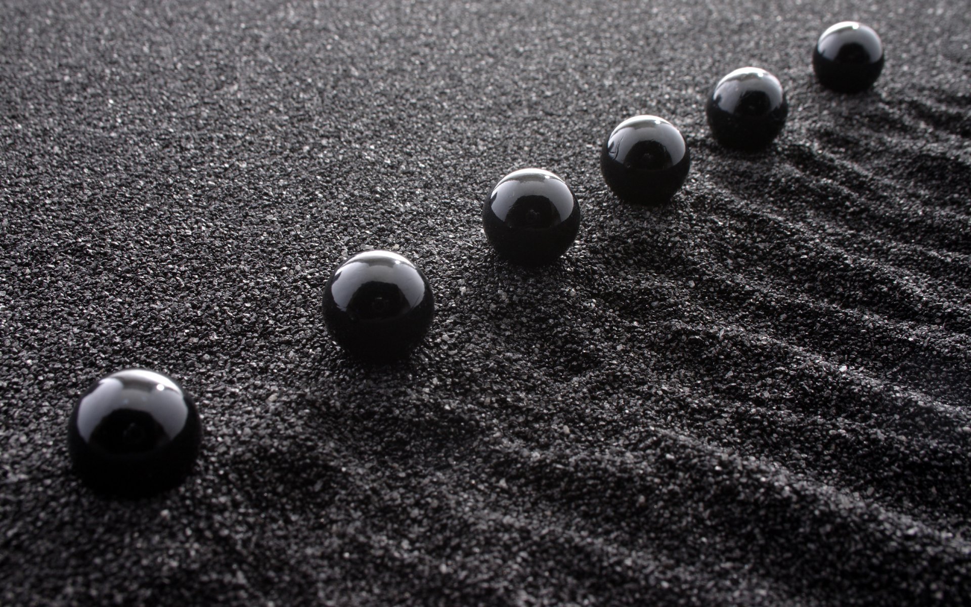 Artistic 3D Art 2K Quad HD PC desktop wallpaper and background showing glossy black spheres in a row on textured black sand with rippled trails.