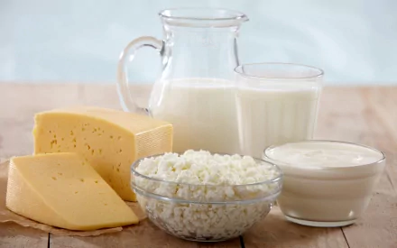 HD desktop wallpaper showcasing a variety of dairy foods: a pitcher and glass of milk, cheese, cottage cheese in a bowl, and a dish of yogurt, set on a wooden surface.