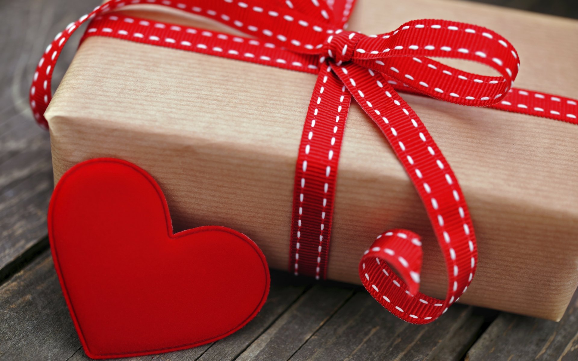 HD PC desktop wallpaper featuring a wrapped gift box with a red stitched ribbon and a red heart, capturing the spirit of Valentine's Day holiday.