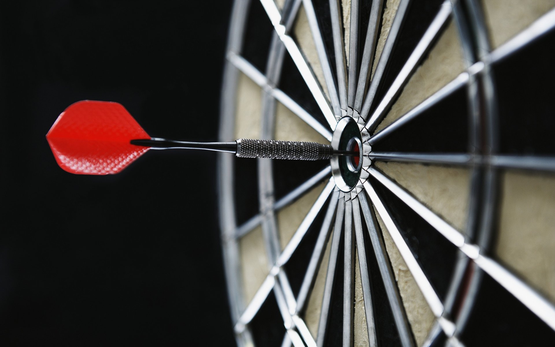 HD desktop wallpaper featuring a close-up of a man-made dart hitting the bullseye on a dartboard against a dark background.
