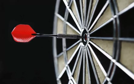 HD desktop wallpaper featuring a close-up of a man-made dart hitting the bullseye on a dartboard against a dark background.